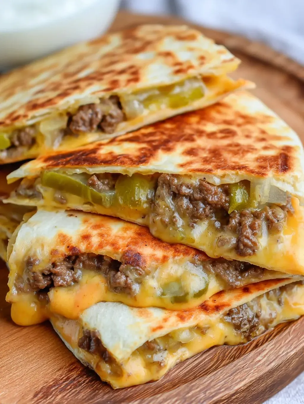 A stack of three tacos with meat and cheese.