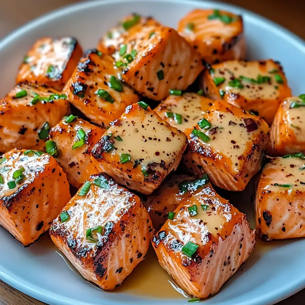 A plate of grilled salmon cubes garnished with green onions and a drizzle of sauce.