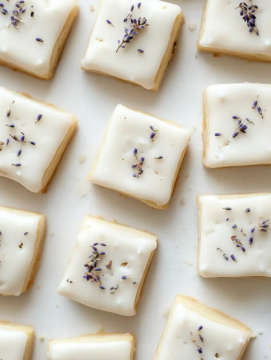 A close-up of small, square cookies topped with white icing and sprinkled with dried lavender flowers.