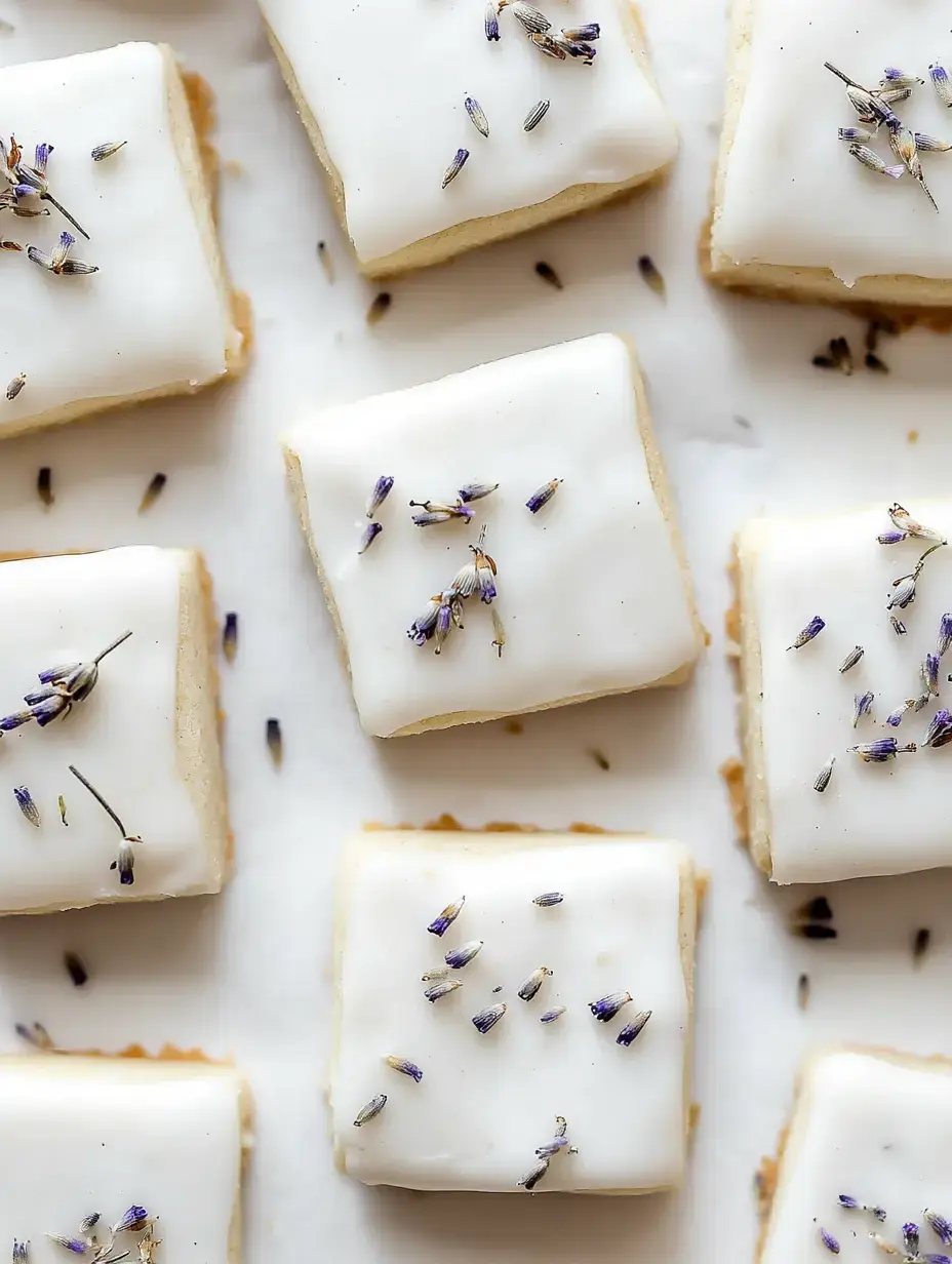 A close-up of square cookies topped with white icing and sprinkled with dried lavender flowers.