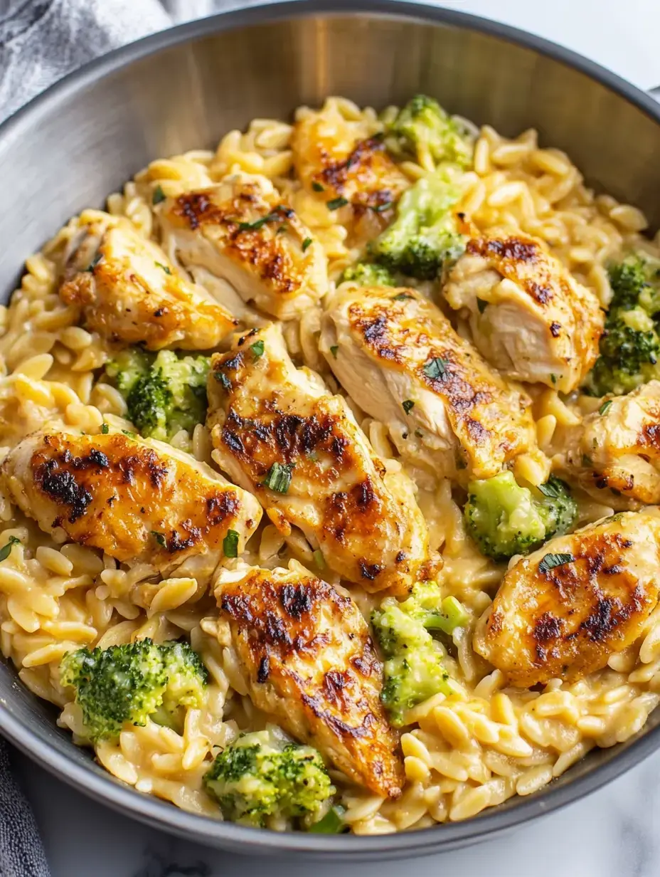 A creamy pasta dish with grilled chicken pieces and broccoli in a metal bowl.