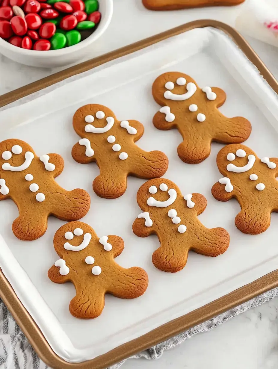 A plate of decorated gingerbread cookies shaped like gingerbread men, adorned with white icing and accompanied by a bowl of red and green candy.