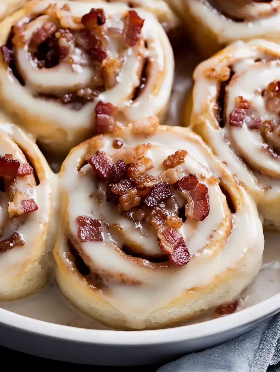 A close-up of freshly baked cinnamon rolls topped with cream frosting and crispy bacon bits.