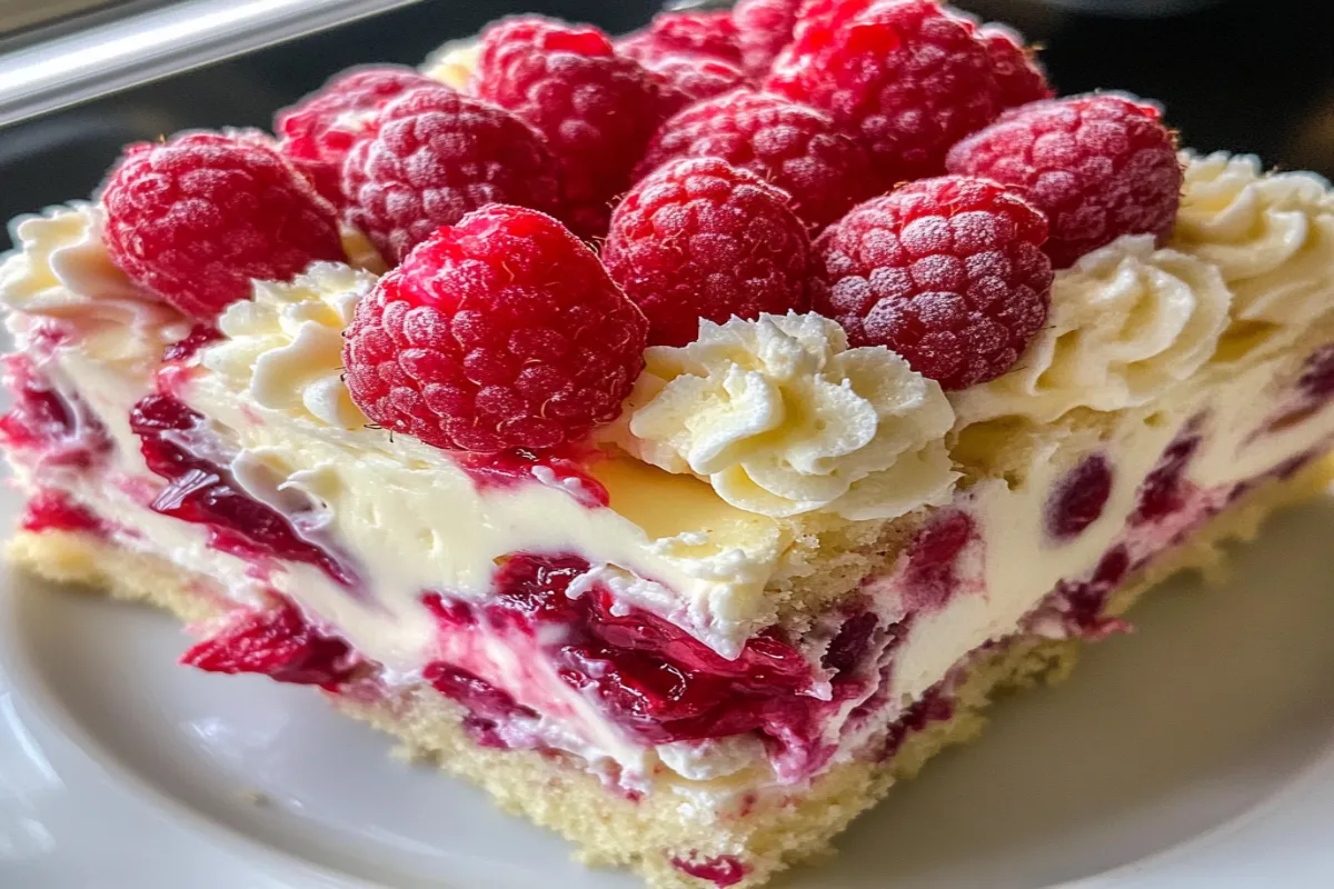 A slice of cake with white frosting and raspberries.