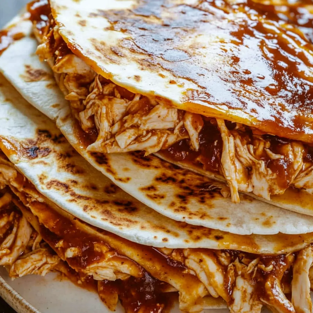 Stacked chicken quesadilla wedges with sauce on the side.