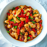 A bowl of chicken with red peppers and green onions.