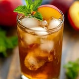 A glass of iced tea with a mint garnish and a slice of peach.