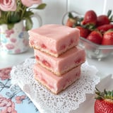 A stack of three pink cakes with strawberries on top.