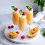 Three glasses of peach juice with raspberries on top.