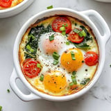 A white bowl filled with eggs, tomatoes, and spinach.