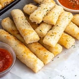 A plate of breadsticks with a bowl of sauce on the side.