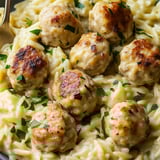 A bowl packed with pasta, meatballs, and veggies.