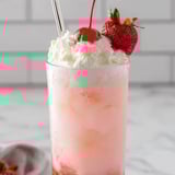 A glass of pink drink with a cherry on top.
