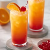 Two glasses of orange juice with cherries on the side.