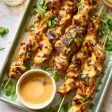 A tray of chicken skewers with a dipping sauce.