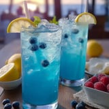 Two blue drinks with lemon and blueberries.