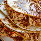 Stacked chicken quesadilla wedges with sauce on the side.