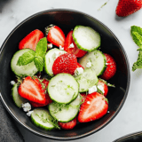 A bowl of fresh fruit with strawberries, cucumbers, and mint.