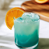 A glass of blue drink with an orange slice on top.