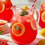 A pitcher of pink lemonade with a lemon slice in it.