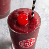 A glass of red drink with a cherry on top.