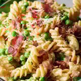 A bowl of pasta with peas and bacon.